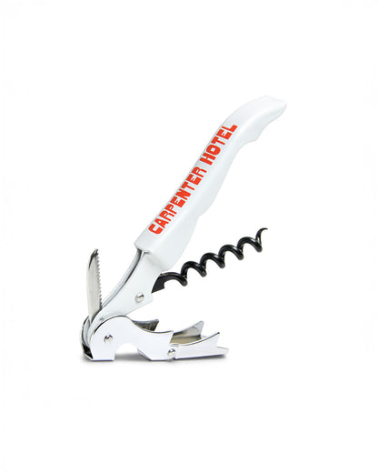 An open silver metal wine key with the Carpenter Hotel logo printed in orange-red on its side.