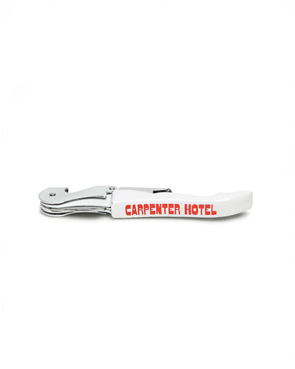 A silver and white metal wine key with the Carpenter Hotel logo printed in orange-red on its side.